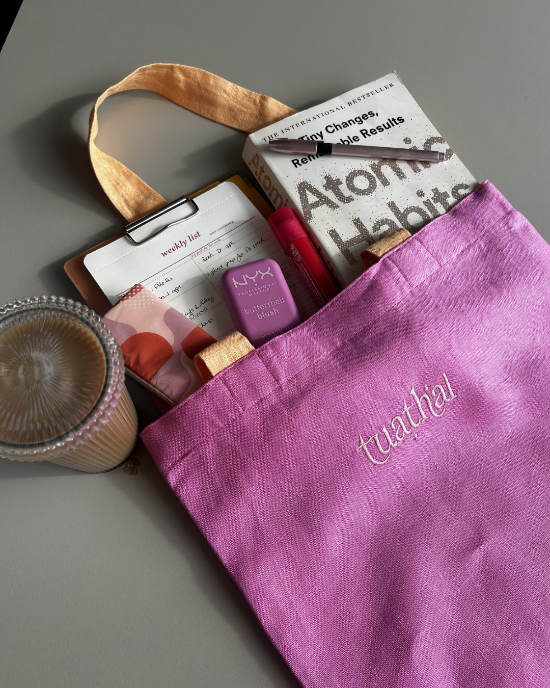 Pink linen tote bag with orange straps lying on a desk, with contents peeking out of the top. 