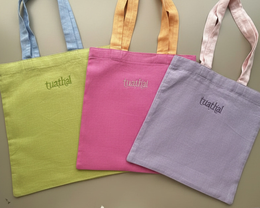 Three Tuathal linen tote bags in green, pink, and purple on desk 