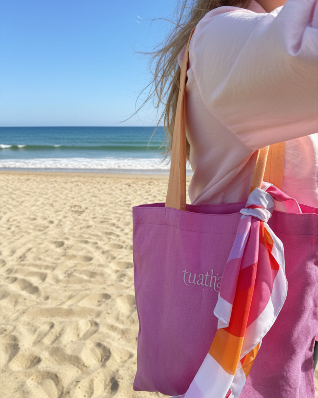 Woman walking on beach carrying pink linen tote bag on shoulder 