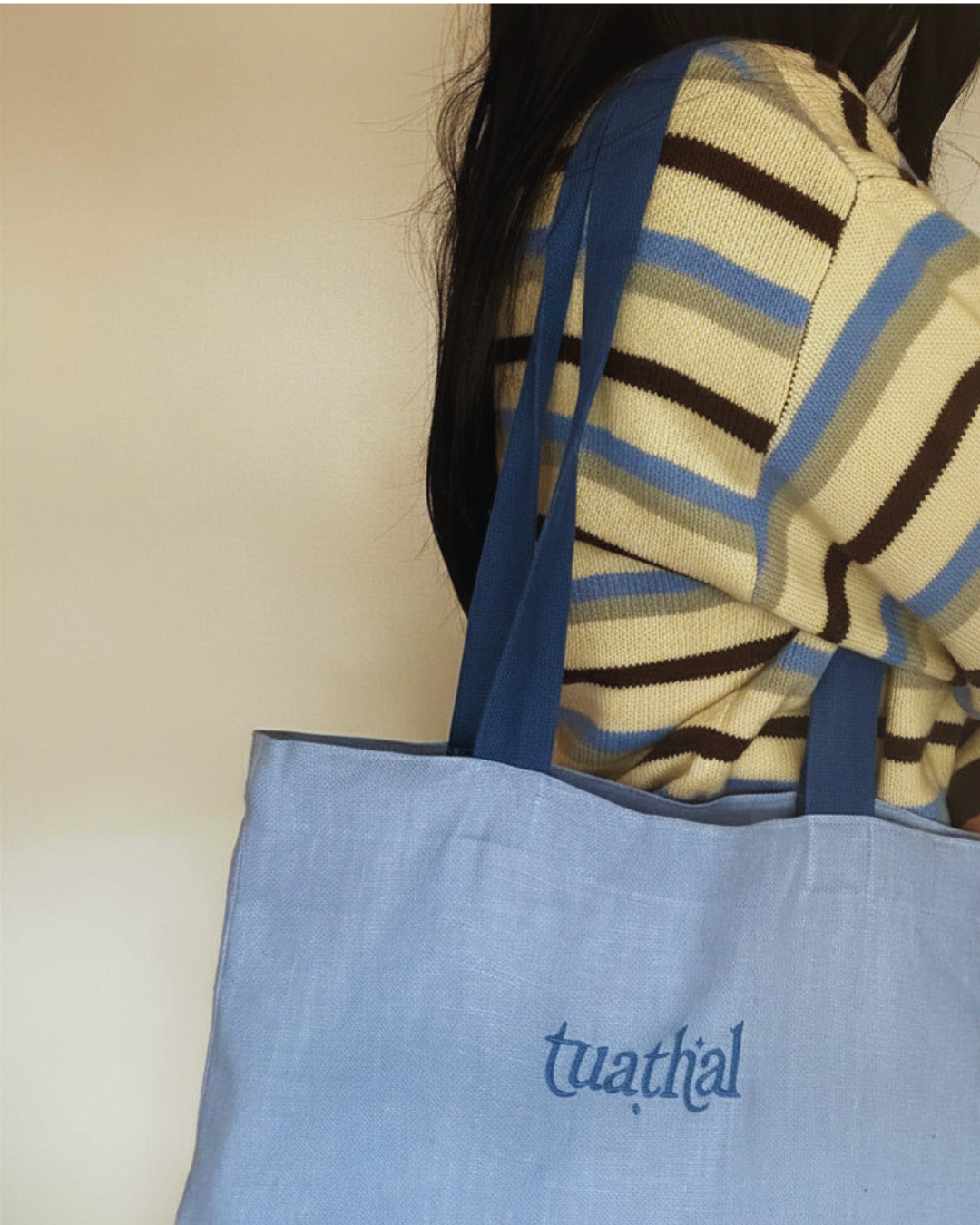 Dark haired woman holding light blue Tuathal linen tote bag in shoulder